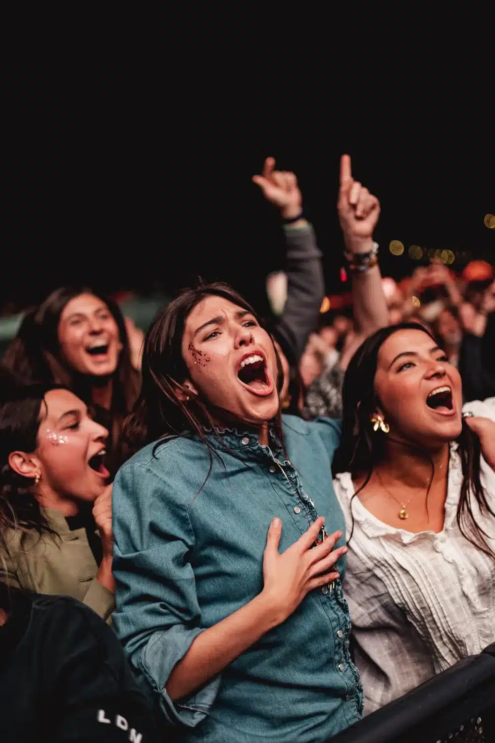 Tres jóvenes gritando y cantando entre el público en primera fila
